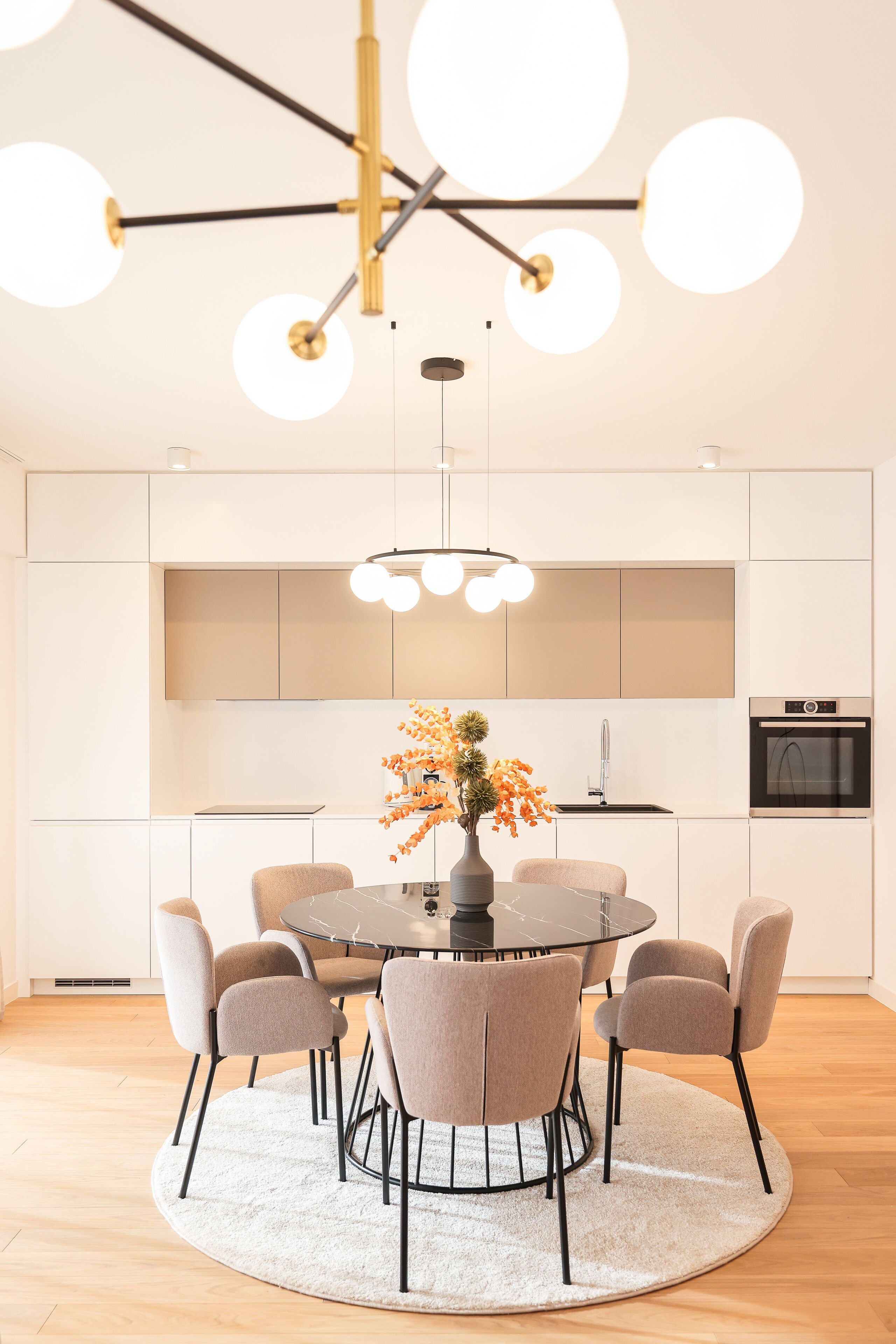 A modern kitchen with white cabinetry, a round dining table, six chairs, and a central island.