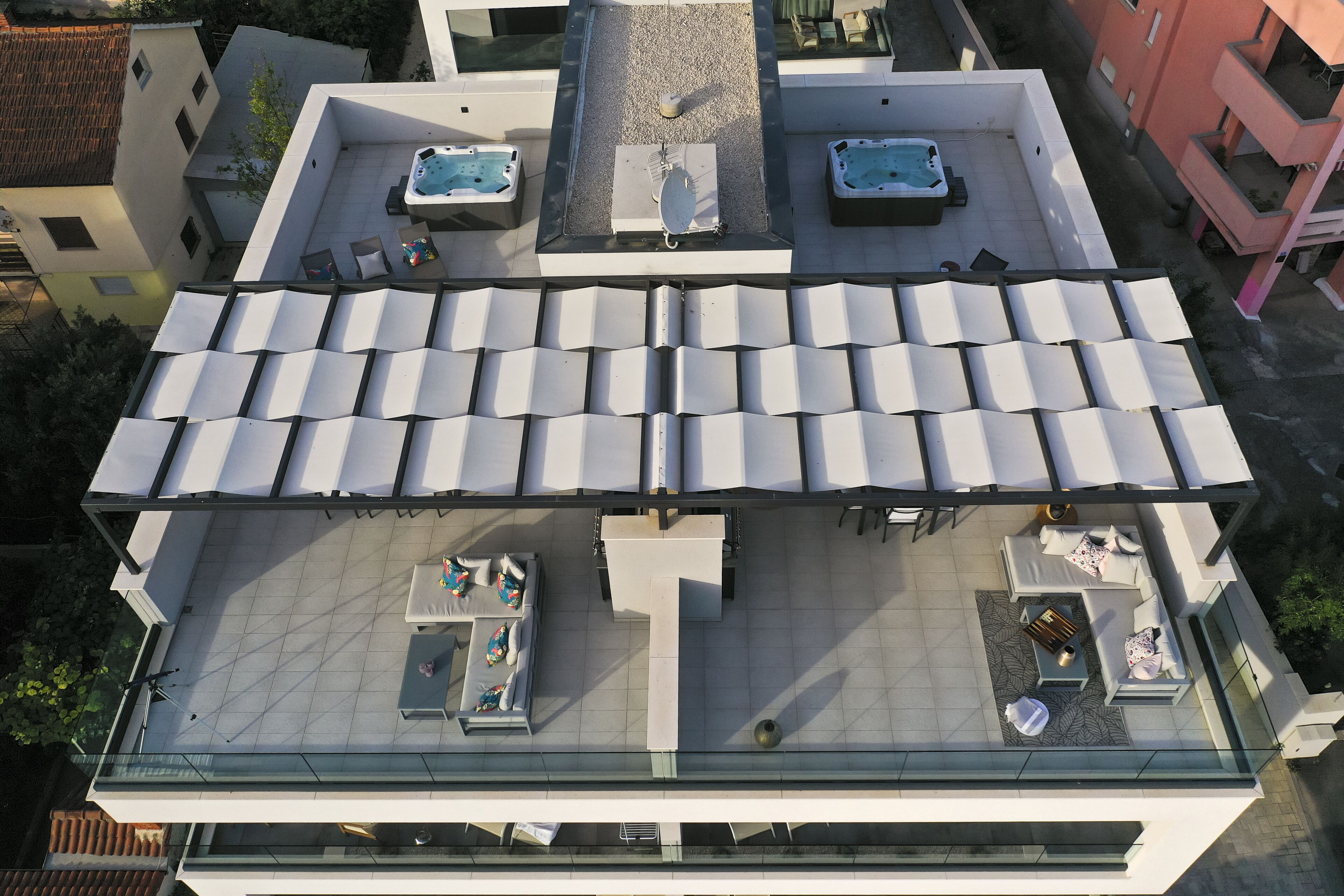 A rooftop terrace with multiple sun loungers, a hot tub, and a seating area with tables and chairs.