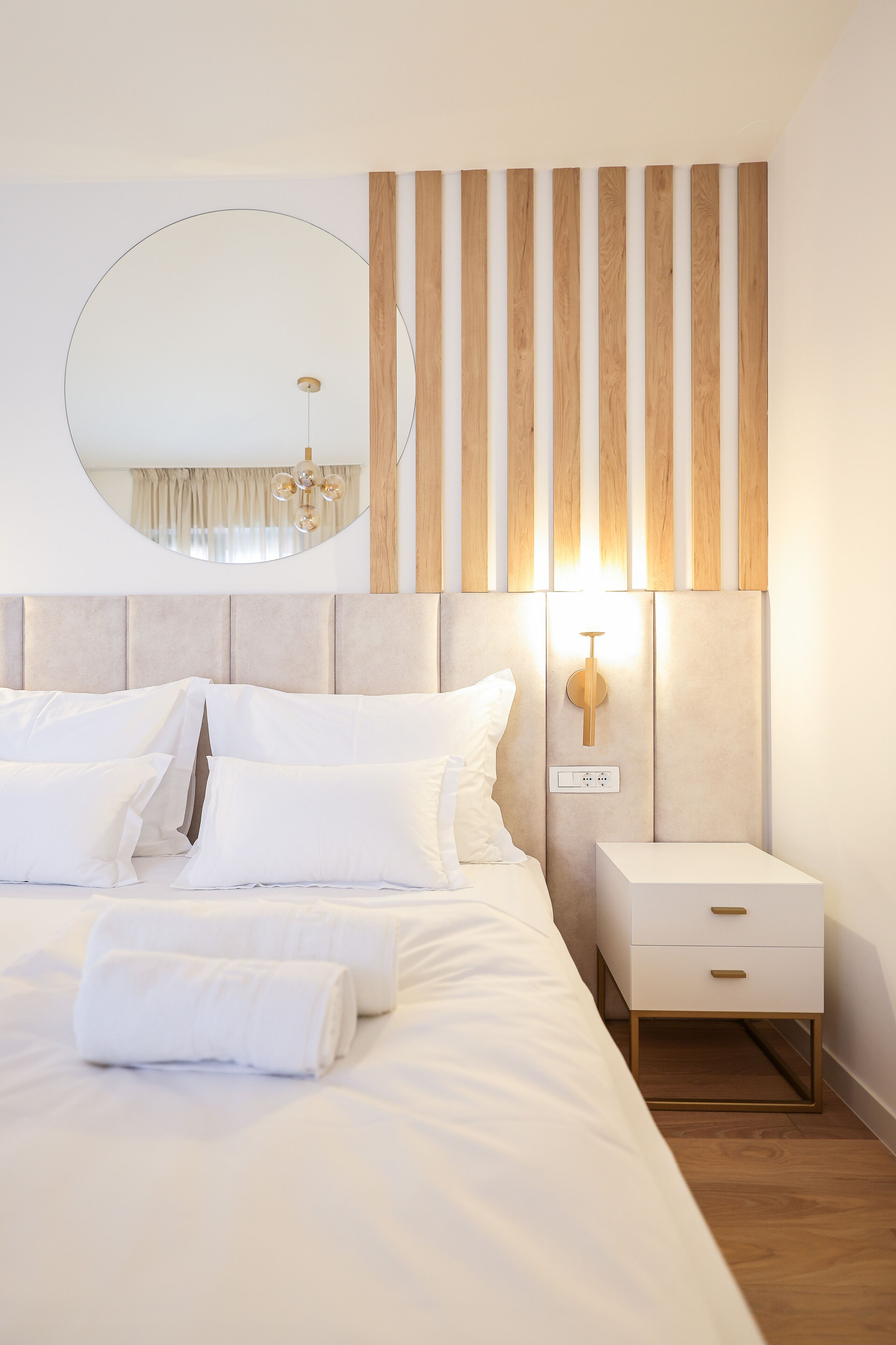 A modern bedroom with a large bed, a bedside table, a wall-mounted light, and a mirror.