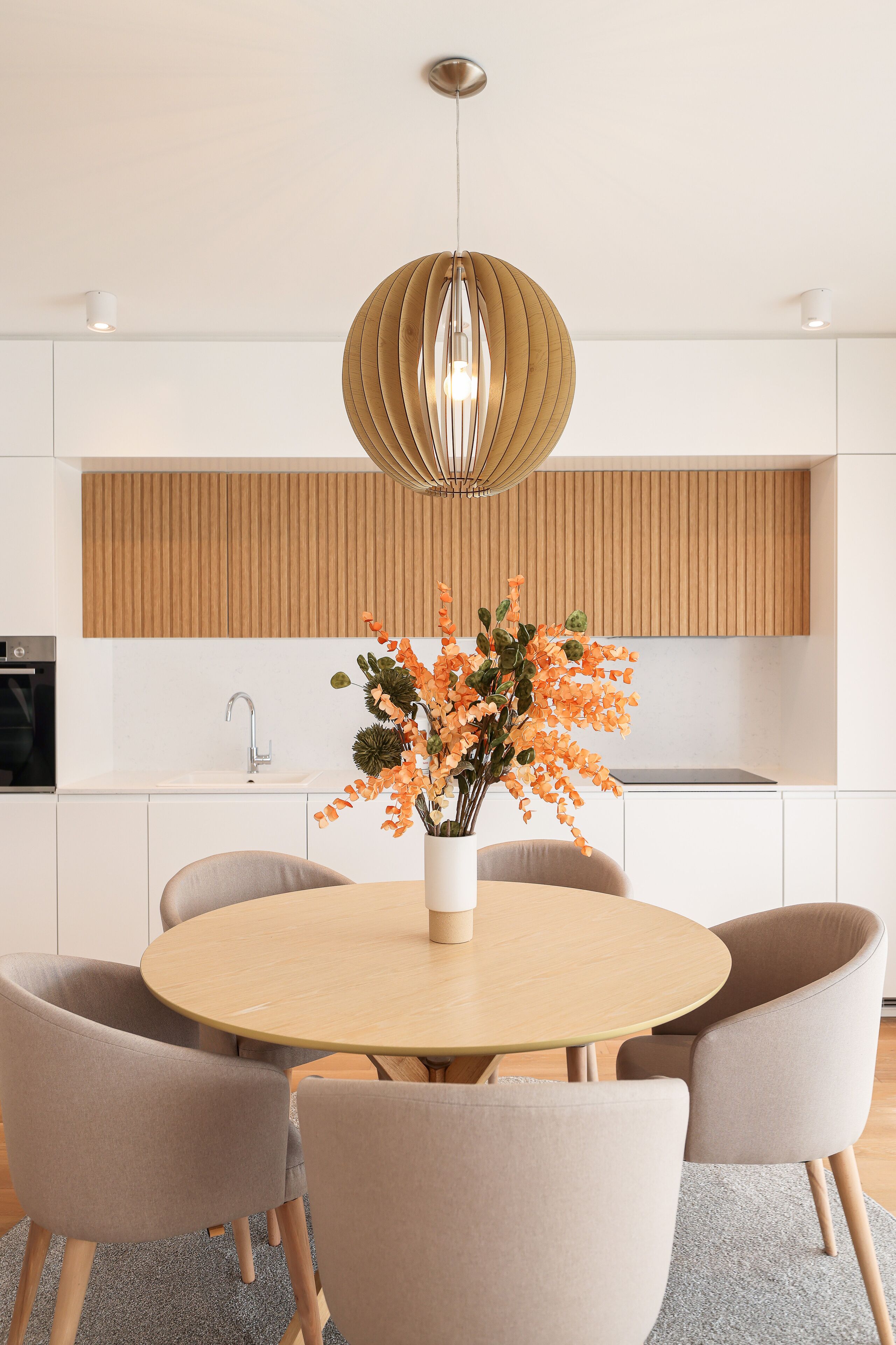 Een moderne keuken met witte kasten, een houten spatwand en een ronde eettafel met stoelen.