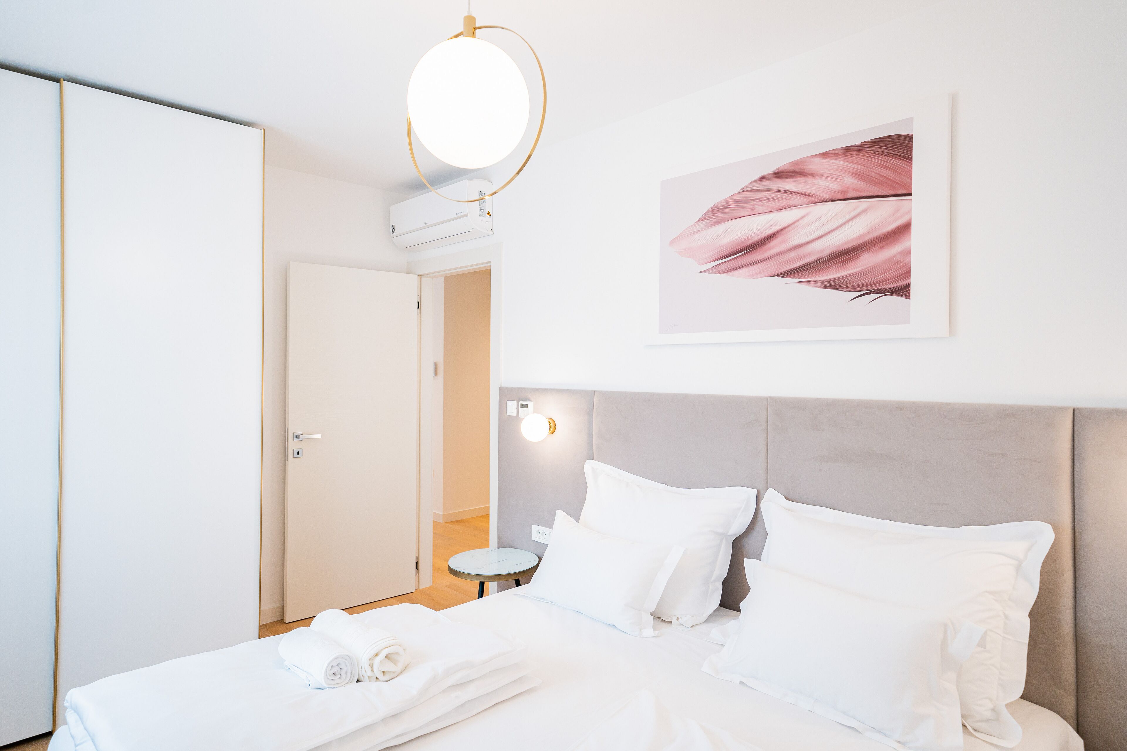 Habitació d'hotel amb llit, almoines, un llum penjant rodona, un aparell d'aire condicionat, una obra d'art emmarcada i una taula petita.