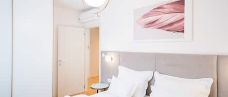 Habitación de hotel con cama, almohadas, lámpara redonda, equipo de aire acondicionado, una obra de arte enmarcada y una mesita.