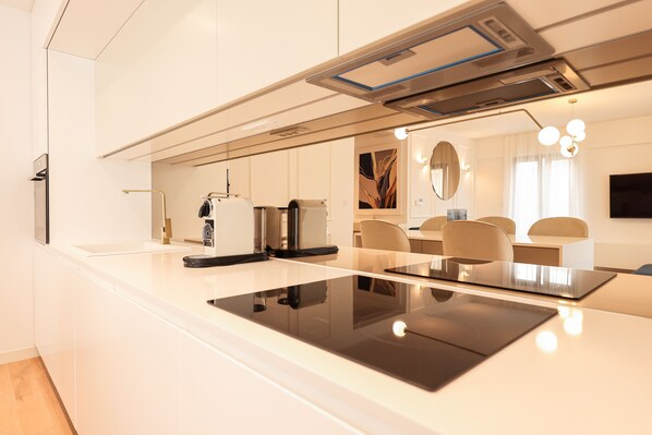 A modern kitchen with a sleek black induction cooktop, white cabinetry, and a minimalist design. - Adria Concept boutique apartments (Zadar)