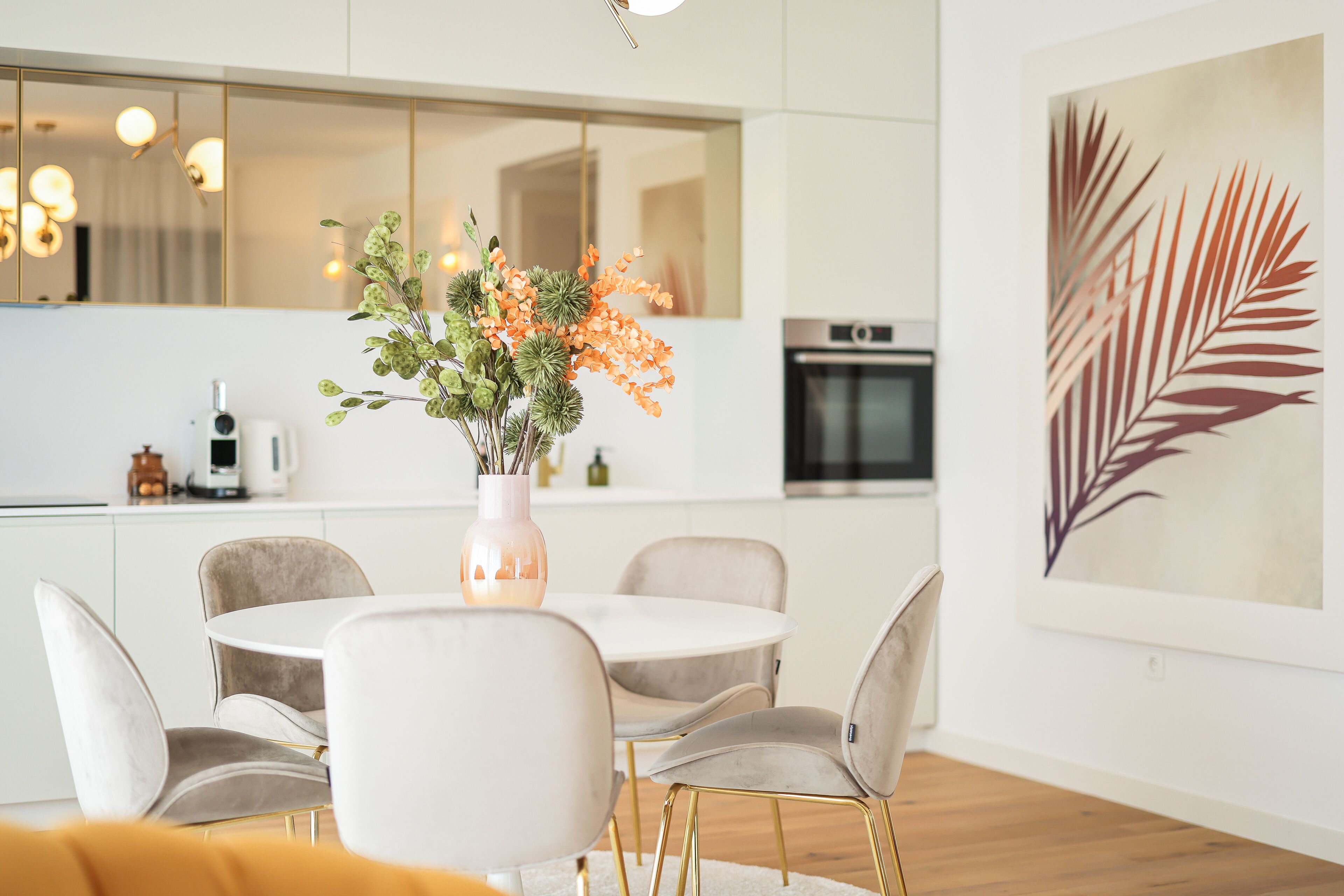 A modern kitchen with white cabinets, a round dining table with chairs, and a vase with flowers.