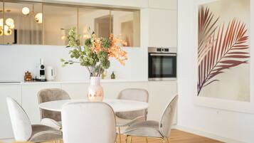 A modern kitchen with white cabinets, a round dining table with chairs, and a vase with flowers.