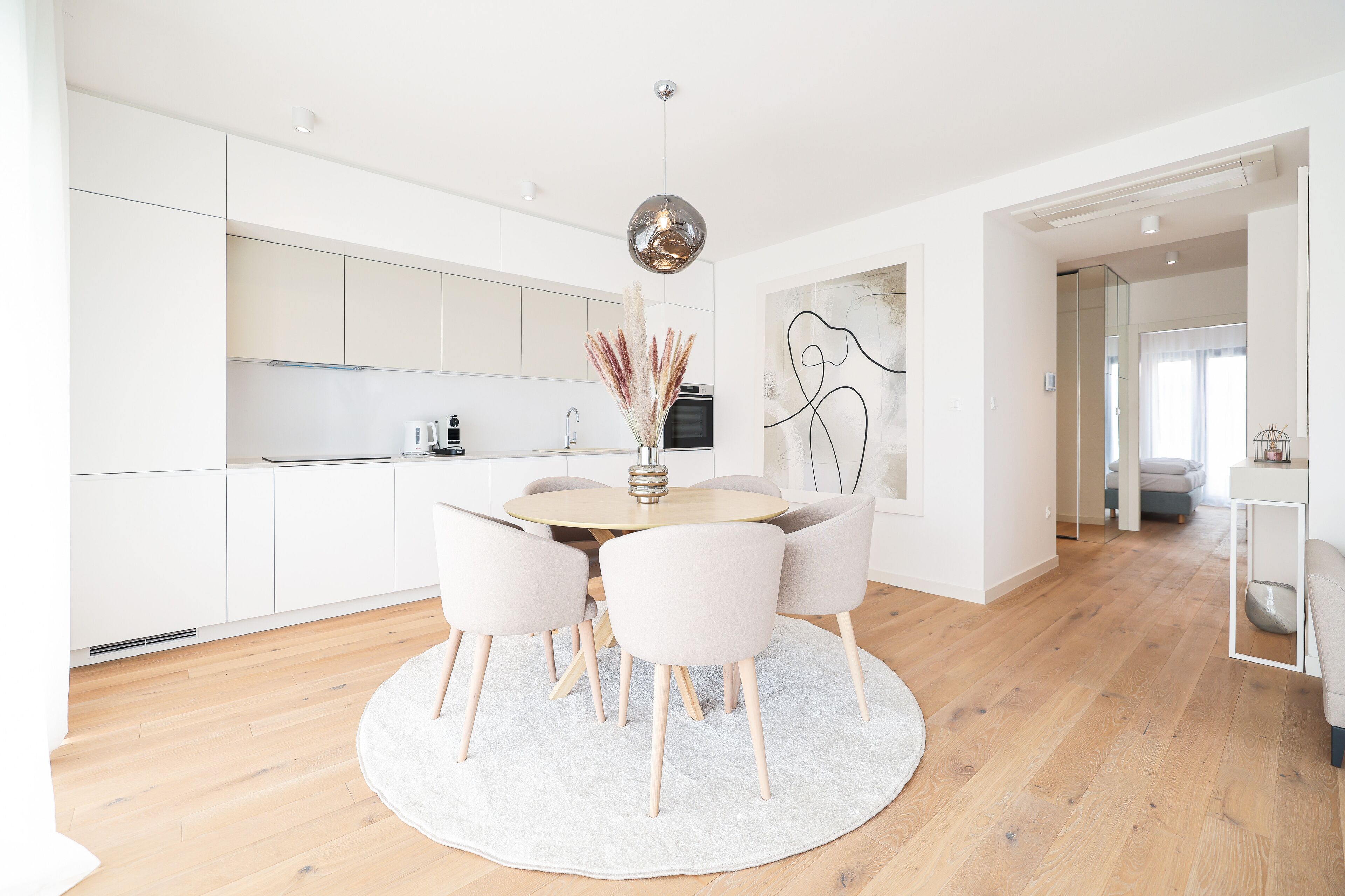 A modern kitchen with white cabinets, a round dining table with chairs, and a hanging pendant light.