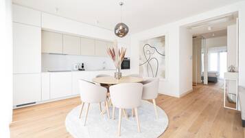 A modern kitchen with white cabinets, a round dining table with chairs, and a hanging pendant light.
