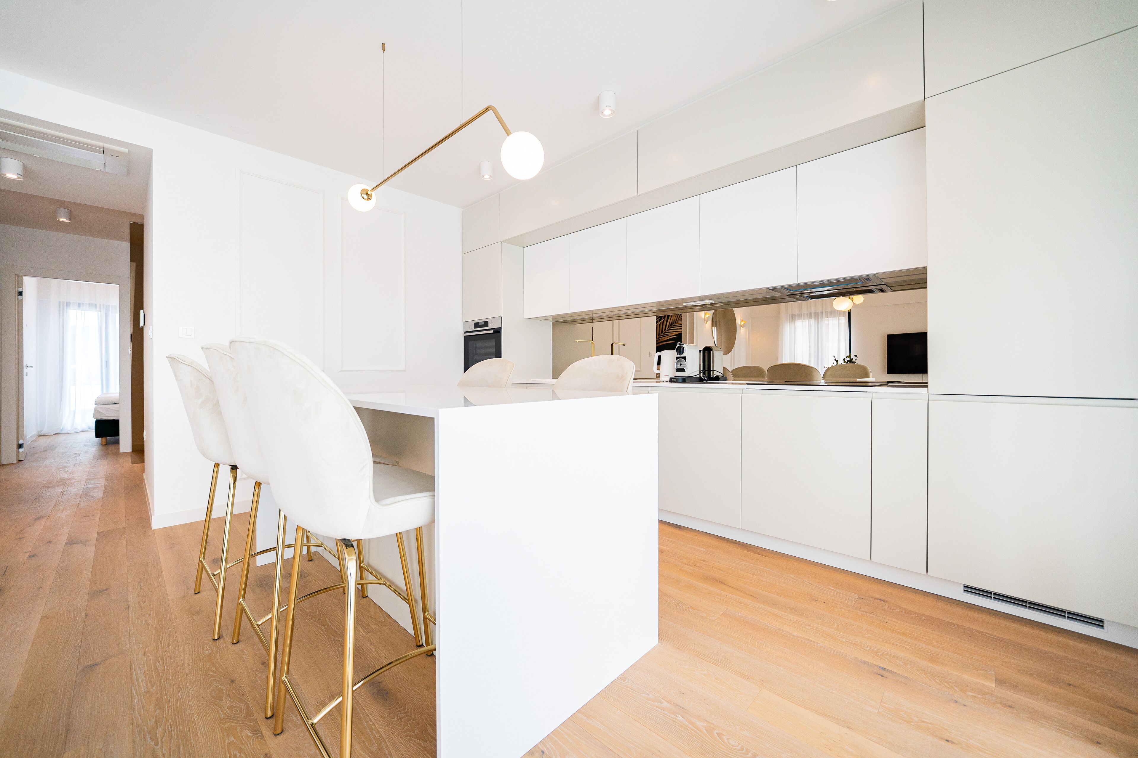 A modern kitchen with white cabinets, a central island with chairs, and a gold pendant light.