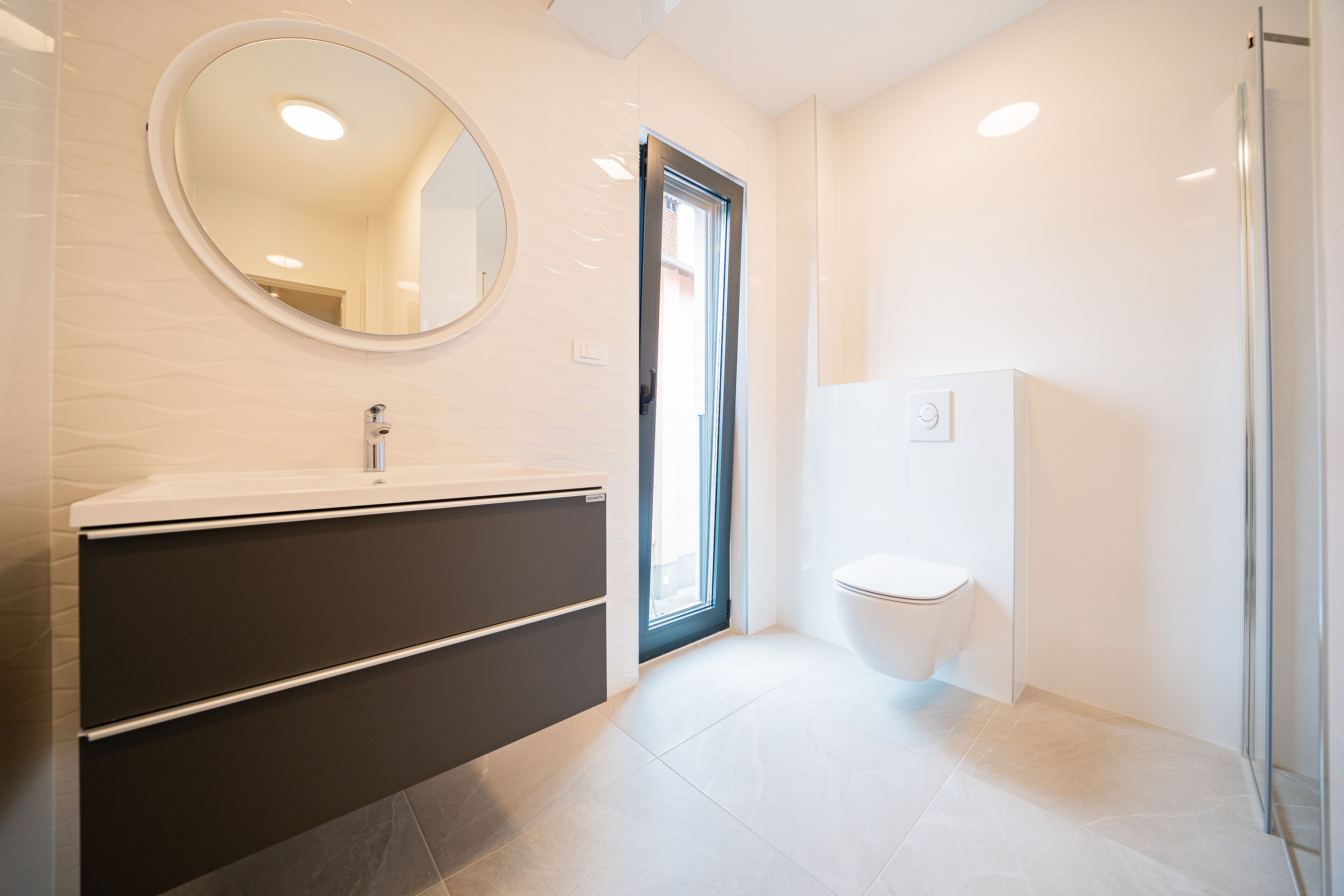 Une salle de bain moderne avec un grand miroir, un meuble-lavabo aux tons foncés, des toilettes et une cabine de douche en verre.