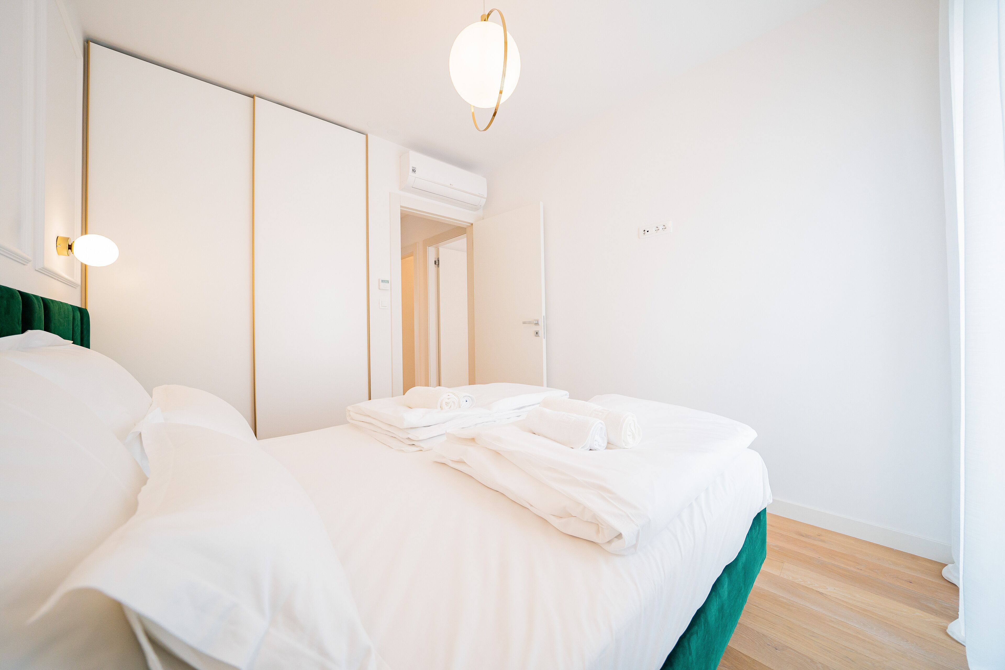 A neatly made bed with white linens, a green accent at the foot of the bed, and a modern light fixture above.
