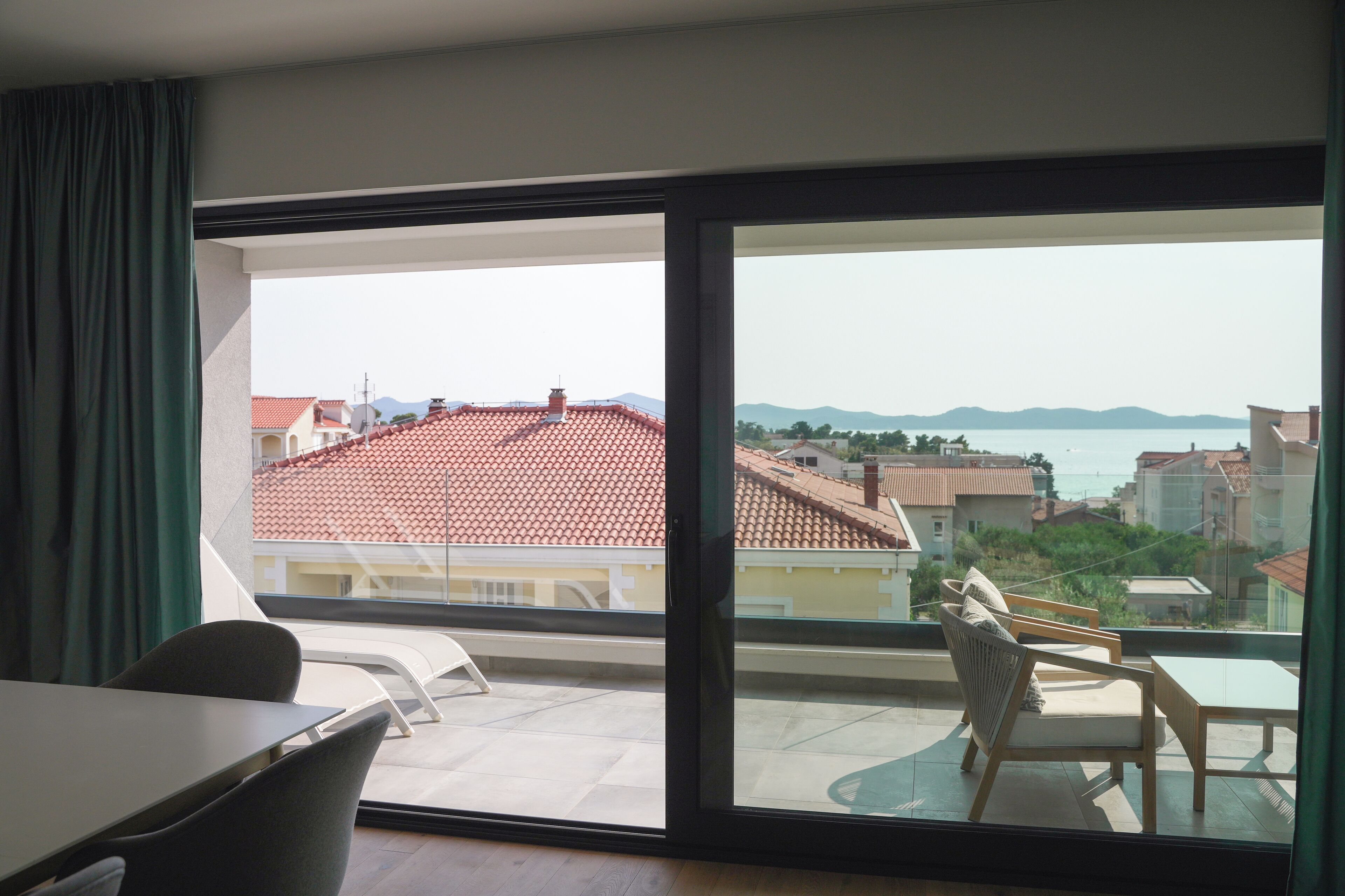 A balcony with a view of a red-roofed building and a body of water.