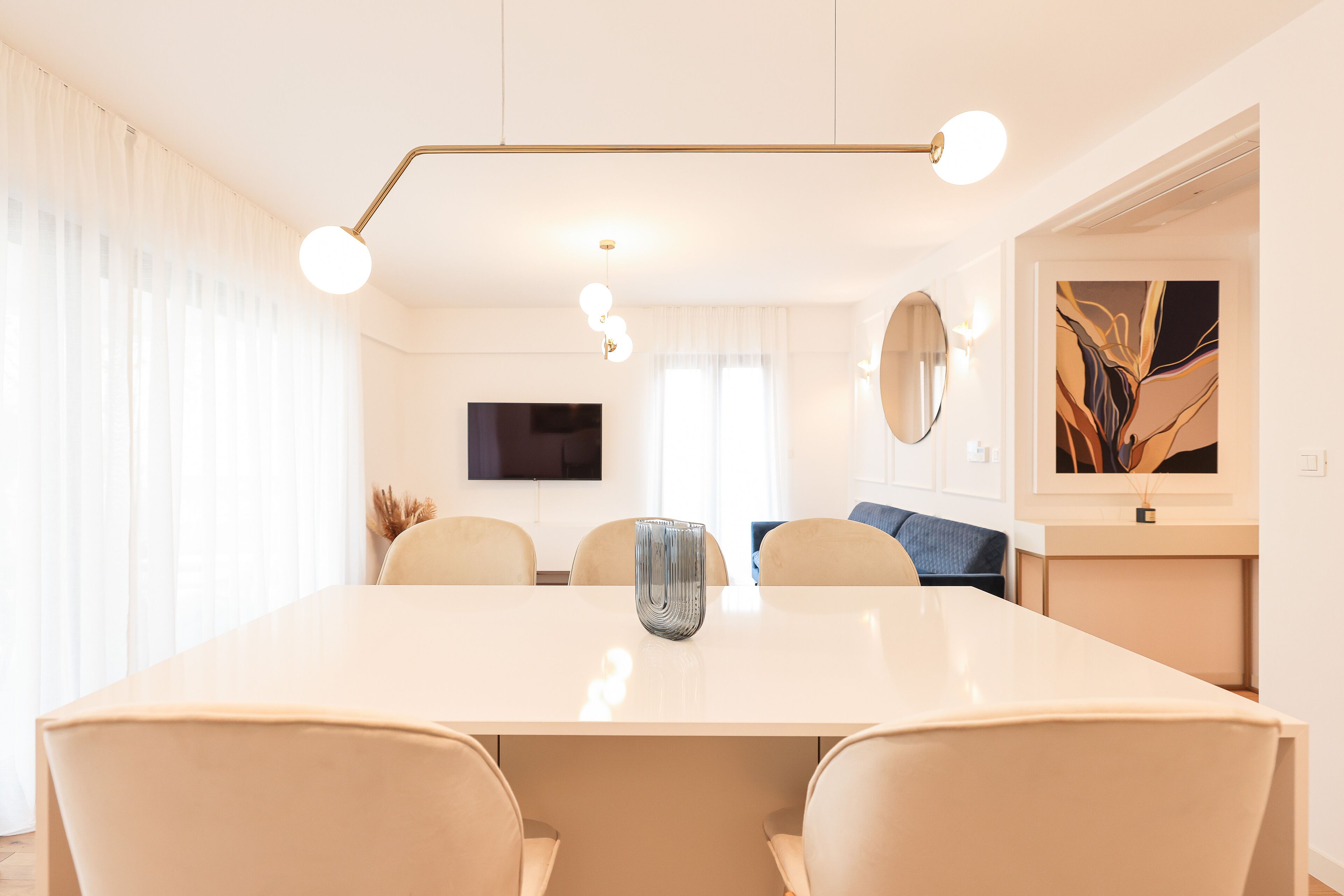 A modern dining area with a large table, four chairs, a vase, and a pendant light.