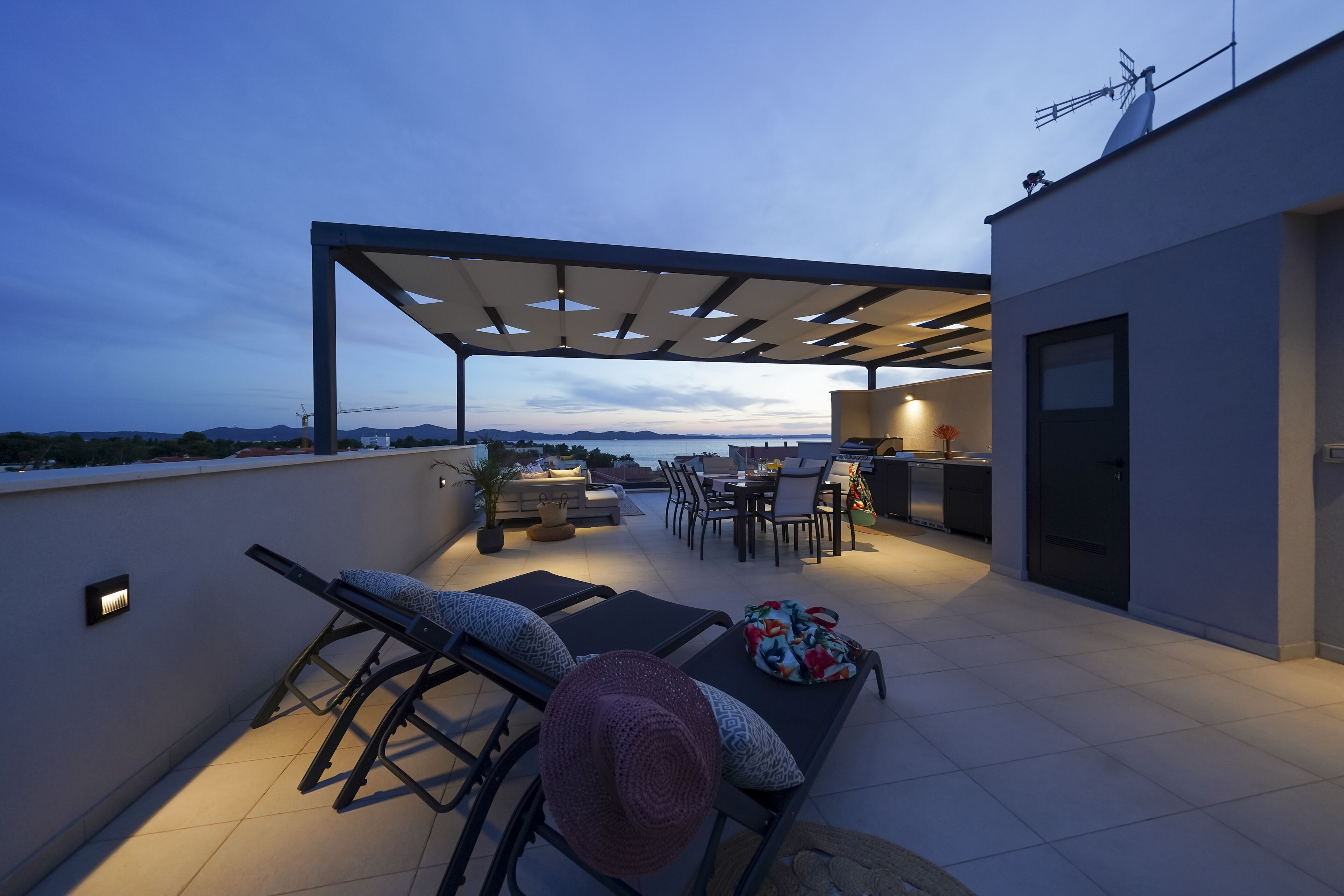 Um terraço no telhado com área de estar coberta, mesa de jantar e cozinha.