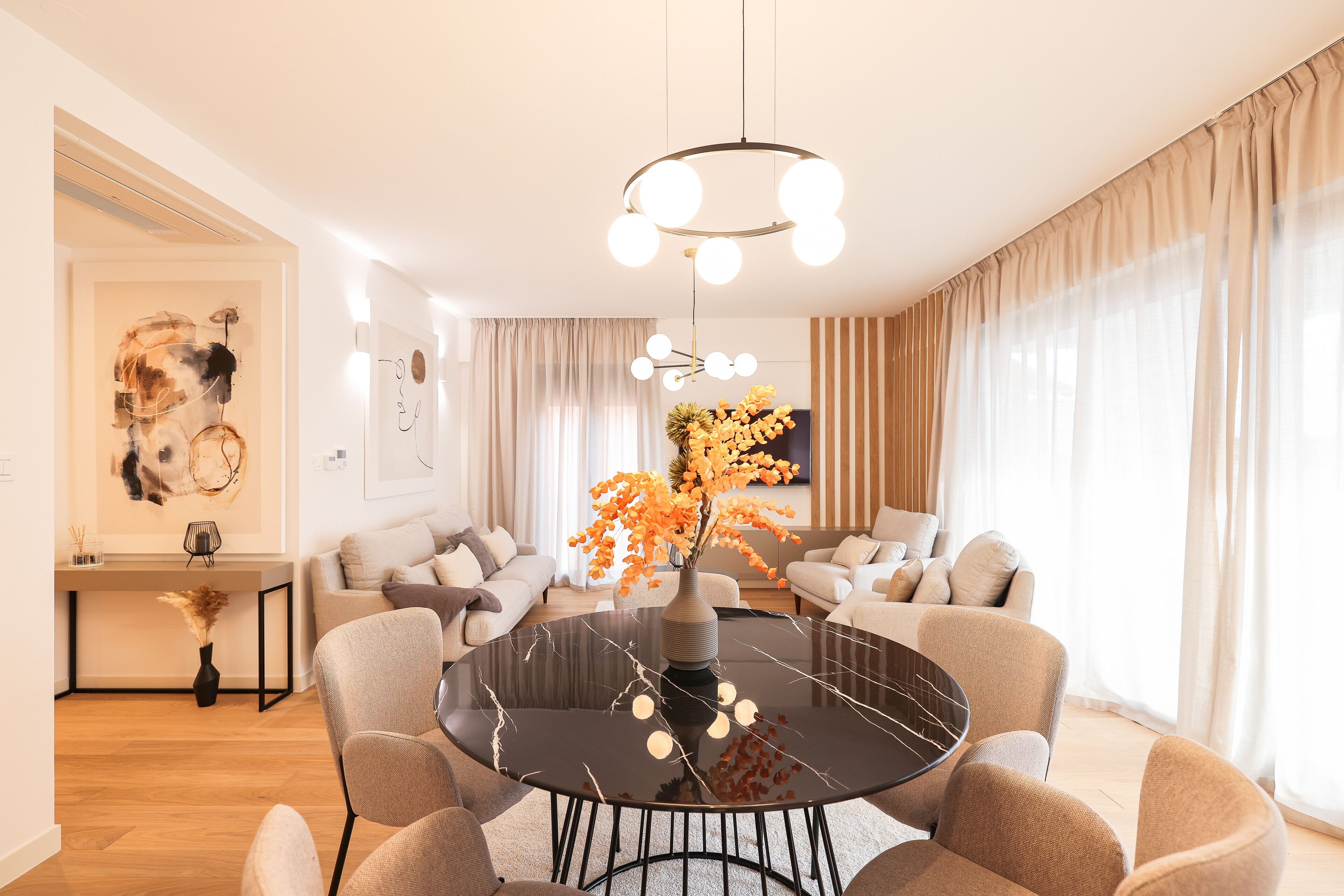 A modern living room with a round dining table, sofas, and a large window with curtains.