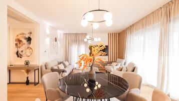 A modern living room with a round dining table, sofas, and a large window with curtains.