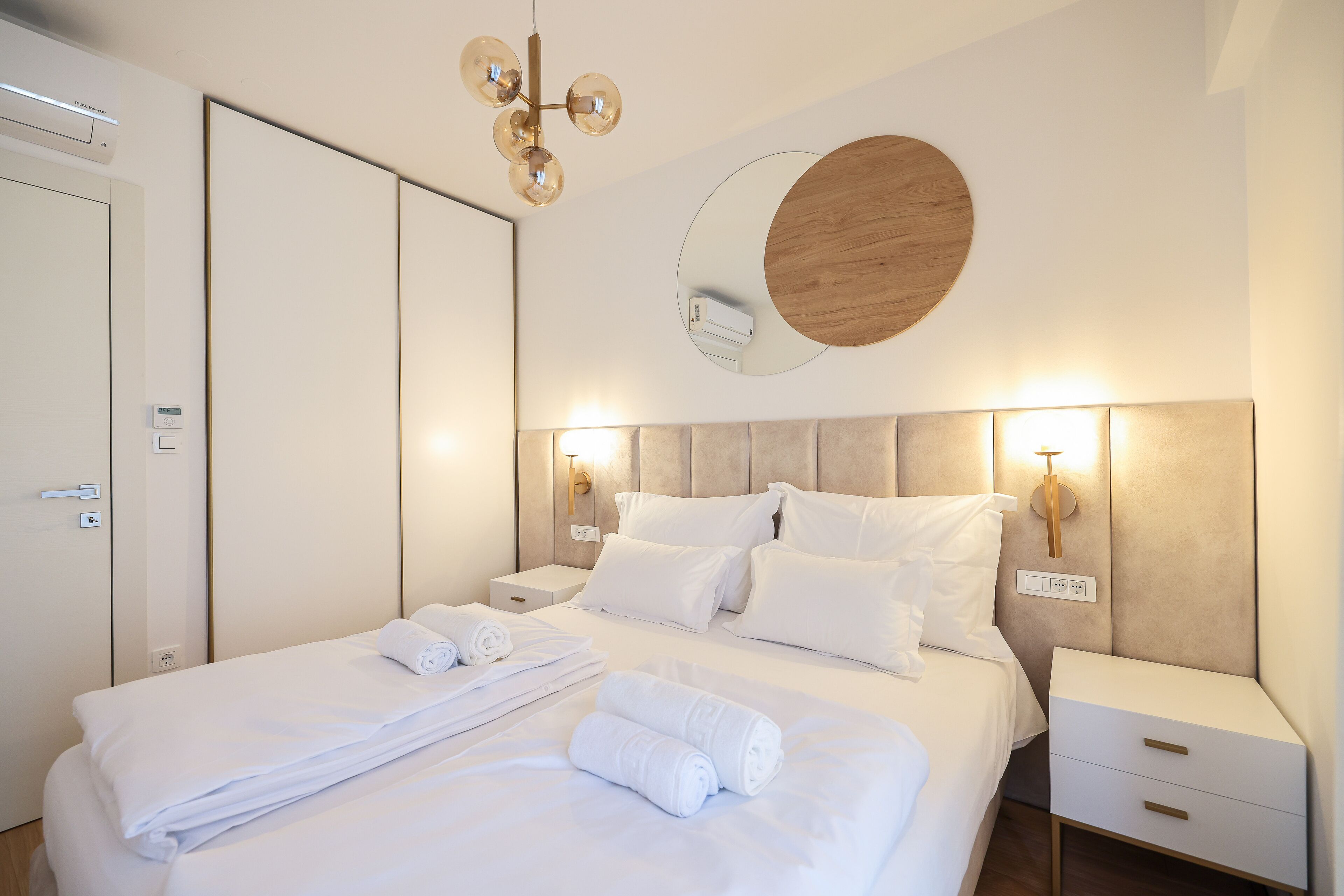 A modern hotel room with a neatly made bed, a bedside table with a lamp, and a wall-mounted mirror.