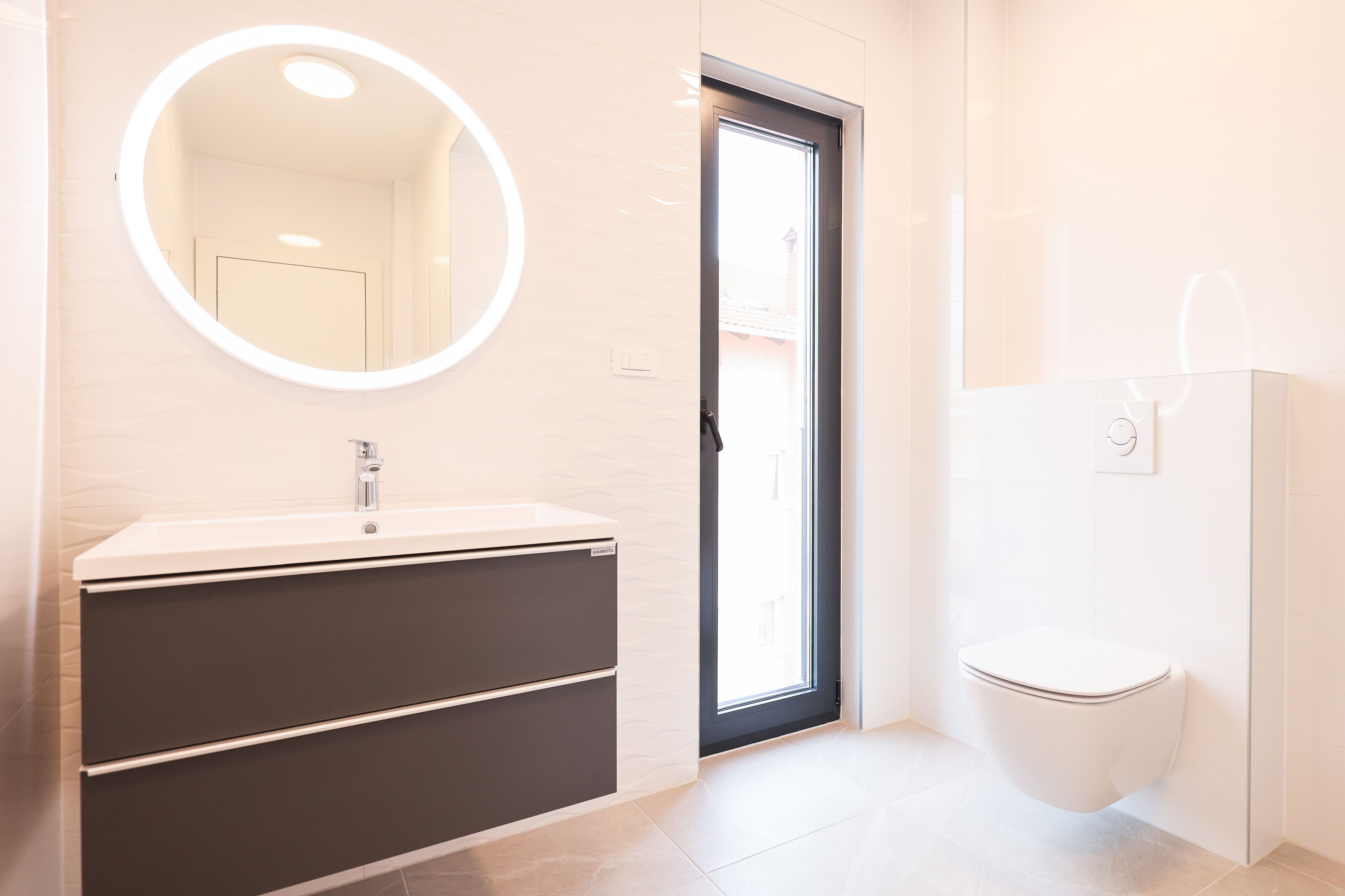 A modern bathroom with a round mirror, a sink with a dark cabinet, and a toilet.