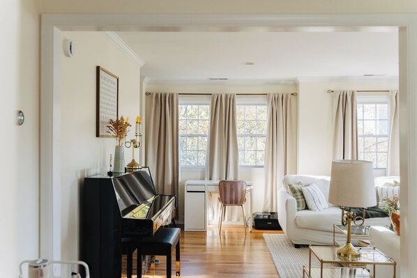 A living room with a piano, a white sofa, a coffee table, and a lamp.