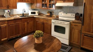 Une cuisine avec des meubles de rangement en bois, un four à micro-ondes, une cuisinière et une table à manger agrémentée d’une plante.