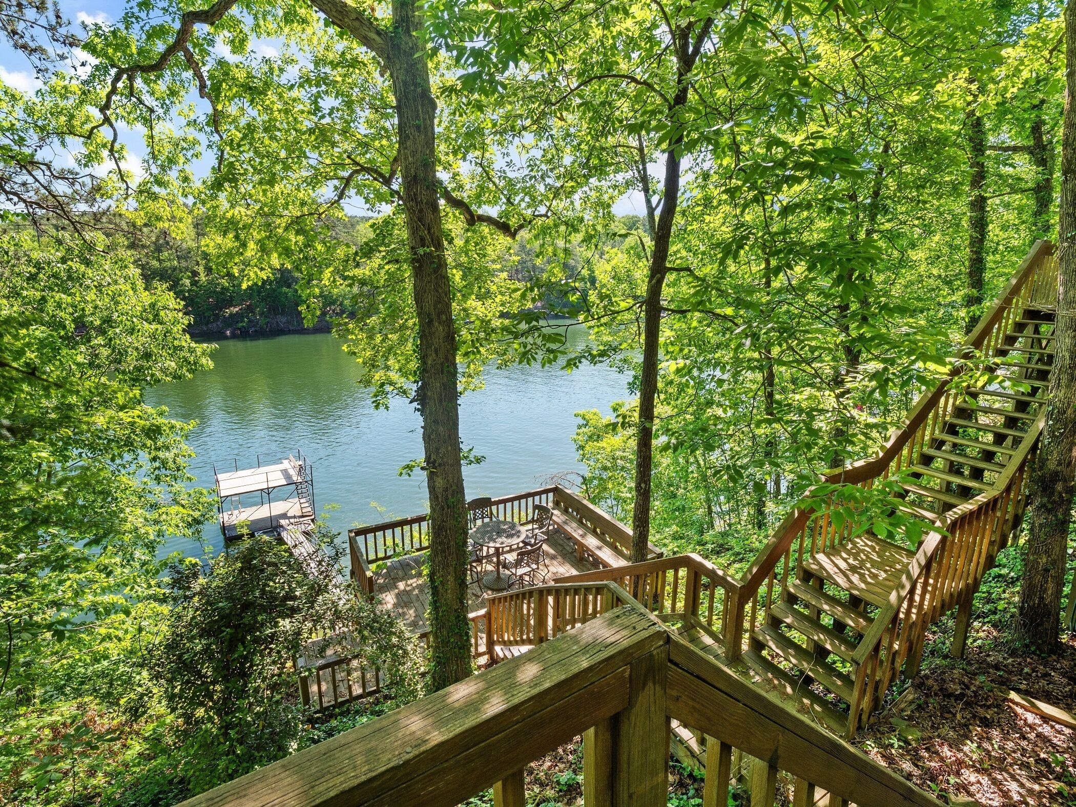 Eine Holztreppe führt zu einem Steg über einen ruhigen See, umgeben von üppiger Vegetation.