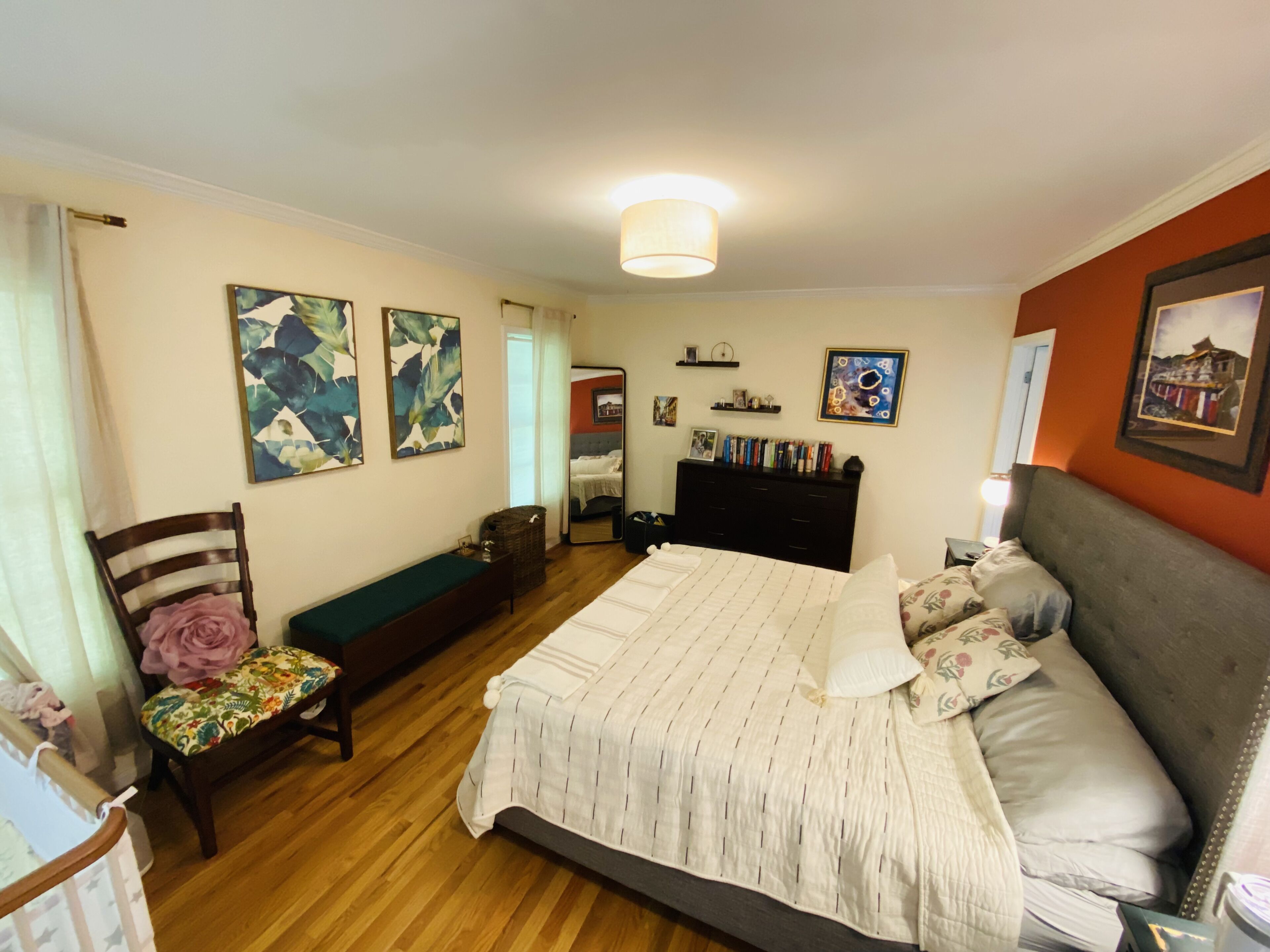 Ein Schlafzimmer mit Bett, einer Bank, einem Sessel, einem Schminktisch und Kunstwerken an den Wänden.