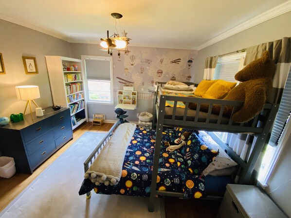 A child's bedroom with bunk beds, a bookshelf, a desk, and a window with curtains.