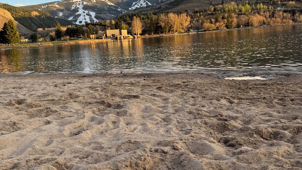 A lake with a sandy shore, a mountain range in the background, and a clear sky.
