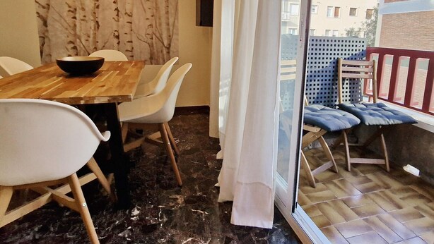 A dining area with a wooden table and white chairs, a black bowl, and a view of a balcony with blue cushions. - Modern apartment close to the Camp Nou Stadium (BARCELONA)
