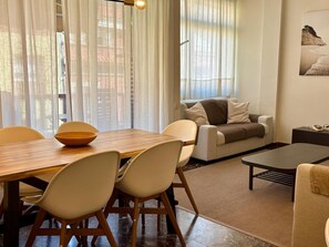 Ein modernes Wohnzimmer mit einem Holzes Esstisch, weißen Stühlen, einer Couch und einem Couchtisch.