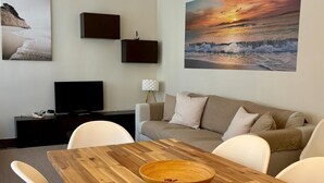 A living room with a wooden dining table, a beige sofa, a TV, and wall art. - Modern apartment close to the Camp Nou Stadium (BARCELONA)