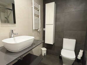 Une salle de bain moderne équipée d’un lavabo sur colonne, de toilettes, d’un porte-serviettes et d’une douche.