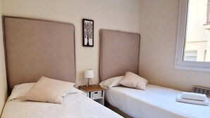 Two single beds with white linens and pillows, a bedside table with a lamp, and a wall art piece. - Modern apartment close to the Camp Nou Stadium (BARCELONA)
