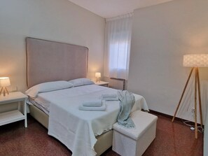 Un lit bien fait, avec du linge de lit blanc, une table de chevet avec une lampe, une petite table de chevet avec une lampe et une lampe sur pied.
