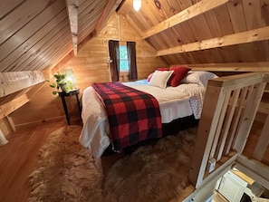 Un dormitorio acogedor en el ático con cama, una mesita con una planta y techo de madera.
