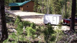 A cabin with a green roof, a garage, and a trailer in a forested area. - Black Hills SD Deadwood, Privacy, Comfort & Convenience with Breathtaking Views (Lead)