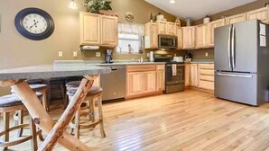 A kitchen with wooden cabinets, stainless steel appliances, a bar area with stools, and a clock on the wall. - Black Hills SD Deadwood, Privacy, Comfort & Convenience with Breathtaking Views (Lead)