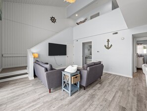Una sala de estar moderna con un sofá gris, un televisor de pantalla plana y decoración náutica.
