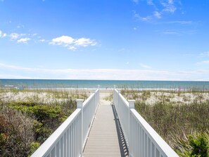 A wooden boardwalk leading to a beach with a clear sky.