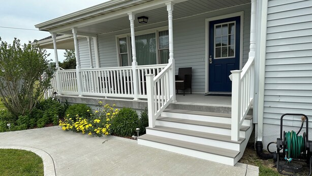 A two-story house with a front porch, a blue door, and a garden with yellow flowers.