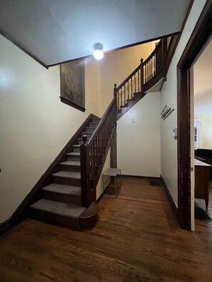 Un escalier en bois avec une rampe, un luminaire au-dessus et une petite table en bas.