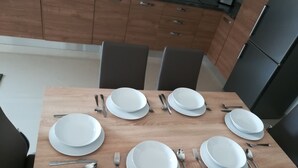 A dining table set for eight with white plates, silverware, and a spoon. The table is in a modern kitchen with wooden cabinets and black chairs. - Modern 2 Bedroom Suite with Kitchen, A/C and Ample Parking (Naxxar)
