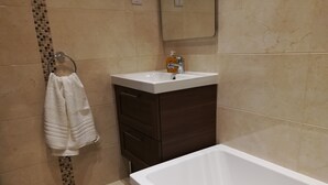 A bathroom with a white bathtub, a sink with a soap dispenser, a towel rack, and a dark-colored vanity cabinet. - Modern 2 Bedroom Suite with Kitchen, A/C and Ample Parking (Naxxar)