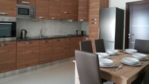 A modern kitchen with wooden cabinets, stainless steel appliances, and a dining table set for four. - Modern 2 Bedroom Suite with Kitchen, A/C and Ample Parking (Naxxar)