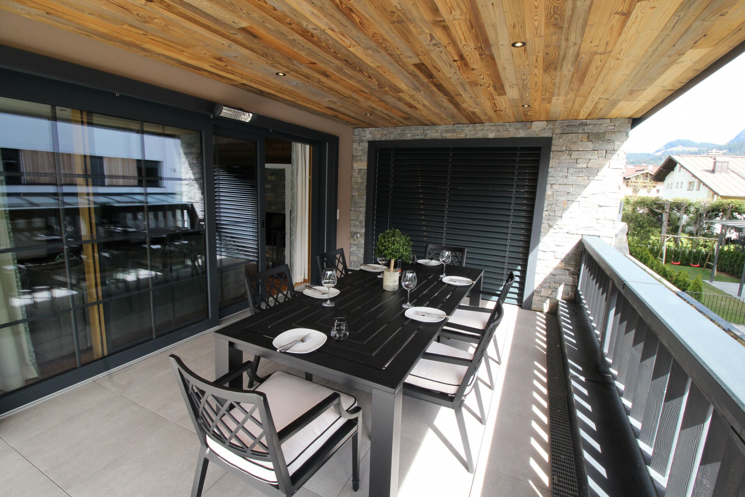 A modern outdoor dining area with a black table and chairs, a potted plant, and a view of the cityscape.