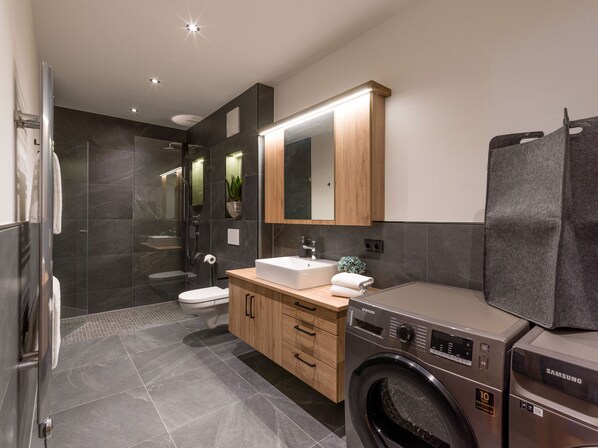 A modern bathroom with a built-in washing machine, a toilet, and a sink. - Bergliebe (Kirchberg in Tirol)
