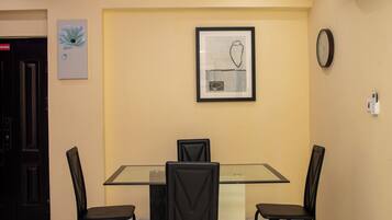 A dining area with a glass table, four chairs, a framed artwork, an air conditioning unit, and a clock on the wall.