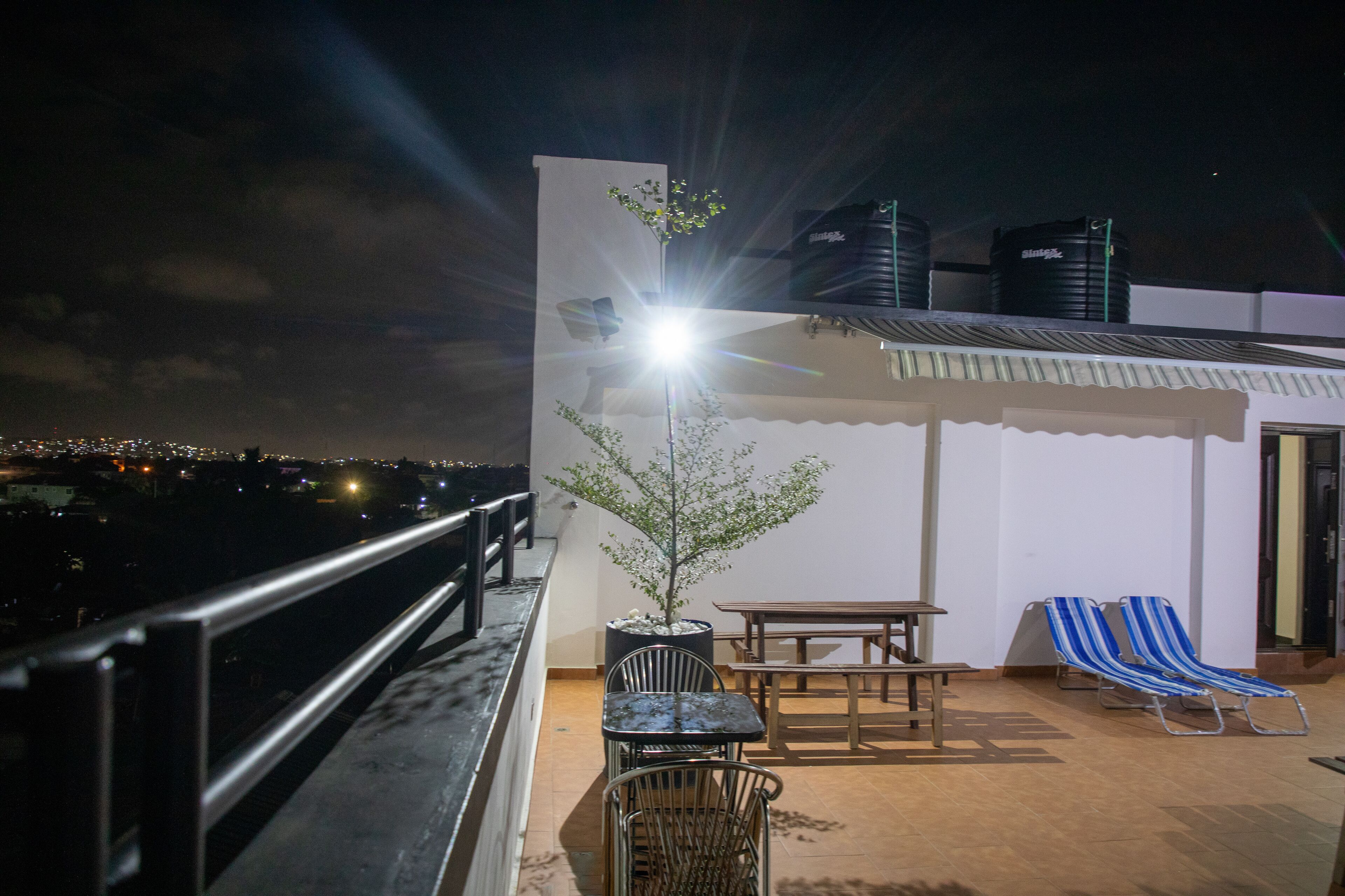 A rooftop terrace with a table, chairs, and a small tree.