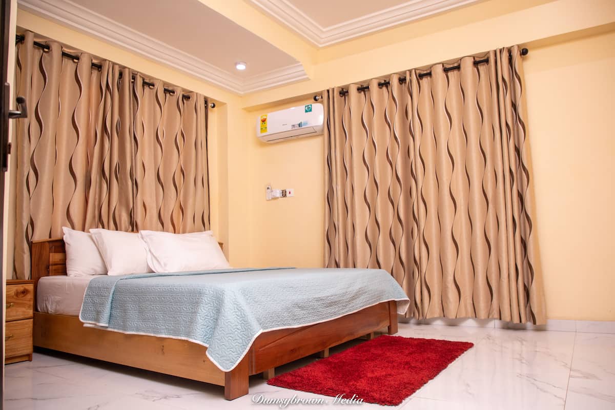A bedroom with a bed, curtains, an air conditioning unit, and a red rug.