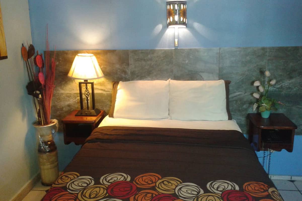 A hotel room with a bed, a nightstand with a lamp, a vase with flowers, and a wall-mounted light fixture.