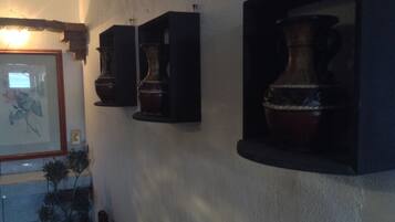 A wall with three dark wooden cabinets, each containing a large ceramic vase. There is a framed picture on the left and a potted plant below the cabinets.